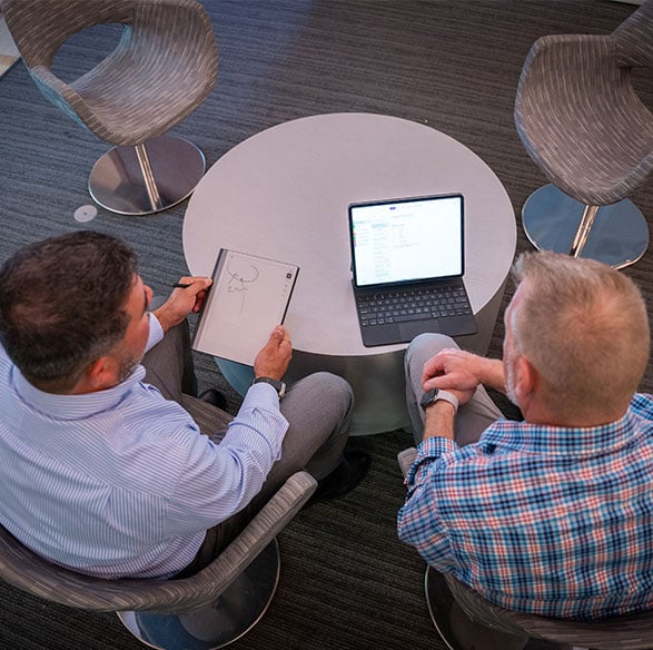 IT professionals collaborating with laptop and digital notepad in modern tech office.